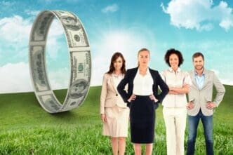 A business team smiles at the camera while standing in a field with a blue sky in the background.