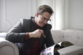 A man in a suit is seated and reading a magazine.