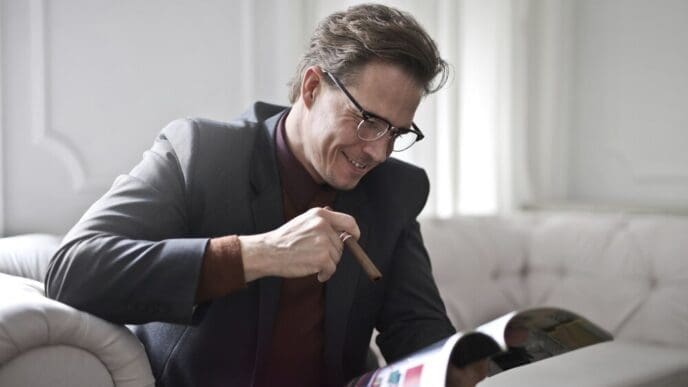 A man in a suit is seated and reading a magazine.