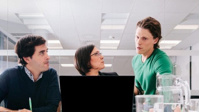 A businessman speaks to a group of coworkers in an office setting.