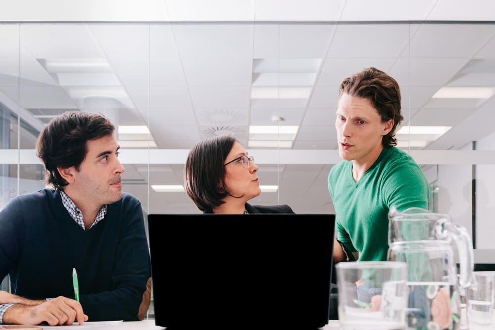 A businessman speaks to a group of coworkers in an office setting.