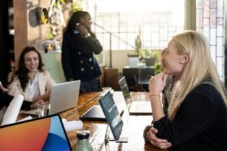 Two businesswomen of diverse ethnicities laugh together in a modern coworking office during a break.