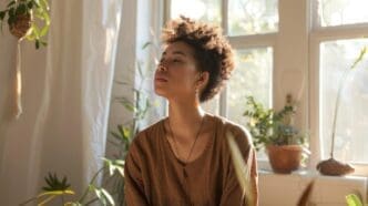 A young woman sits calmly in a brightly lit room filled with plants, exuding tranquility.