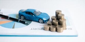 A toy car sits on a stack of coins, illustrating concepts of car loans, savings, and financial planning.