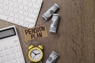 A flat lay shows a card with "Pension Plan" written on it, surrounded by banknotes, a calculator, and an alarm clock on a wooden office table.