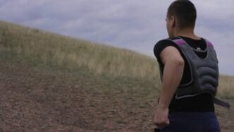 A Caucasian man runs uphill on a steep, dusty trail in a mountainous, arid environment.