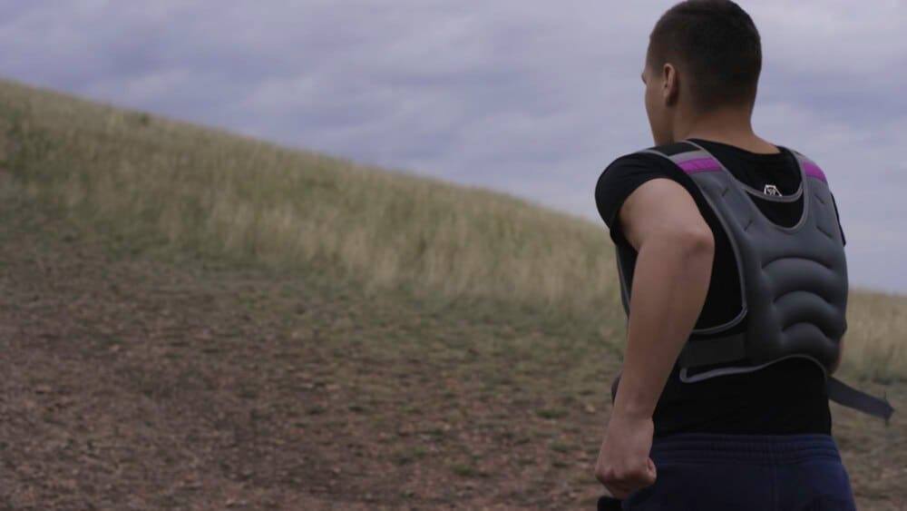 A Caucasian man runs uphill on a steep, dusty trail in a mountainous, arid environment.