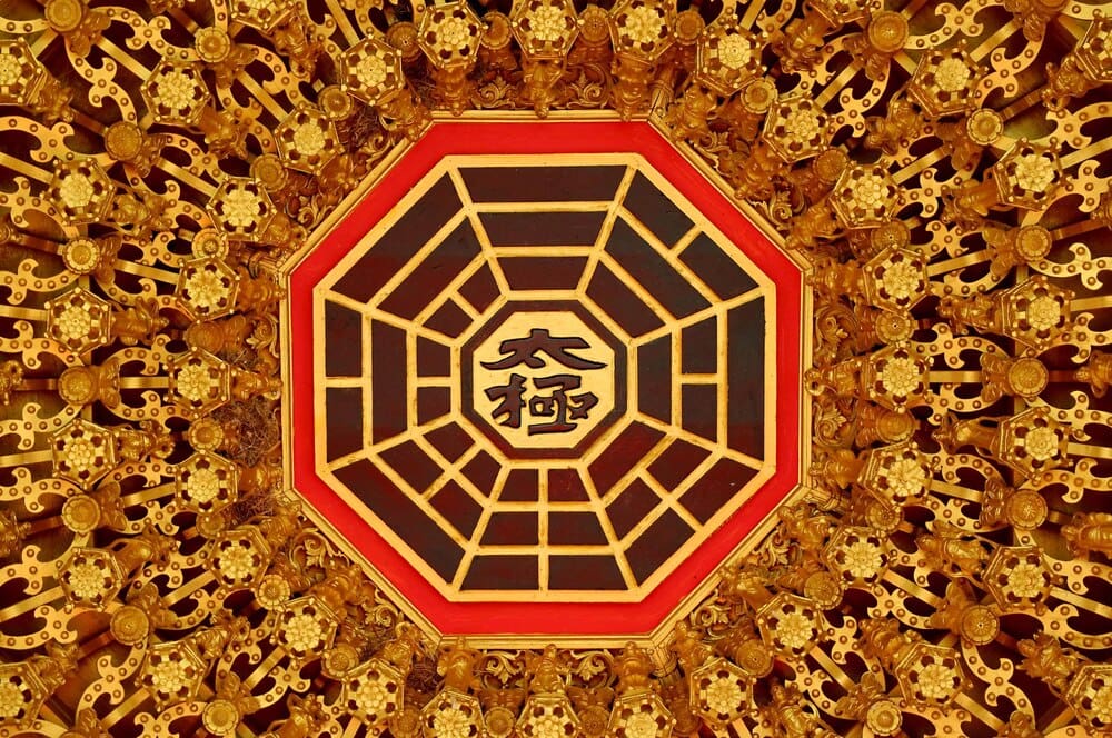 Ornate wood carving on a temple ceiling depicts a Chinese scene with the words "TAI CHI" inscribed, representing the Supreme Ultimate.