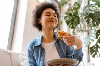 A Black woman with curly hair closes her eyes while enjoying a croissant.