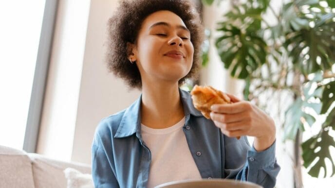 A Black woman with curly hair closes her eyes while enjoying a croissant.
