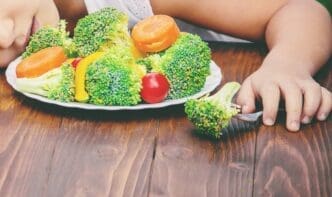 A child with selective focus is shown eating vegetables in a summer photo.