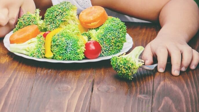 A child with selective focus is shown eating vegetables in a summer photo.