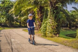 A young child rides a kick scooter in a sunny park.