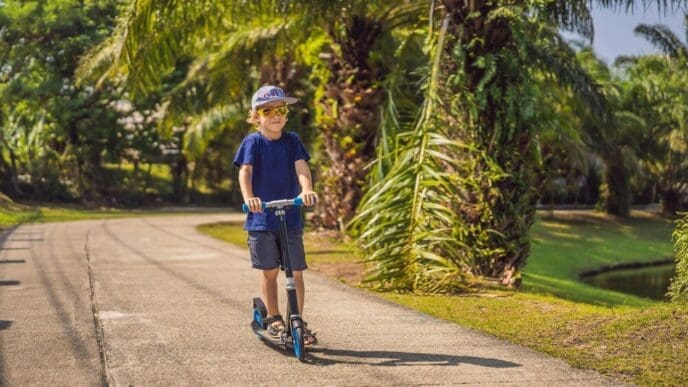 A young child rides a kick scooter in a sunny park.