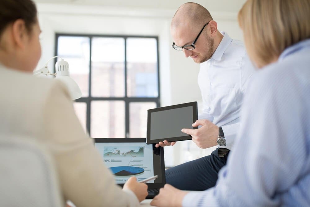 Close-up of a business team gathered around a tablet computer in an office setting.