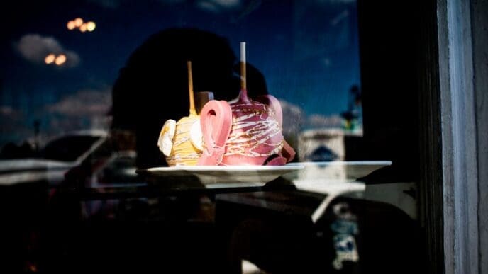 Close-up of a red candy apple on a white plate is seen through a window.