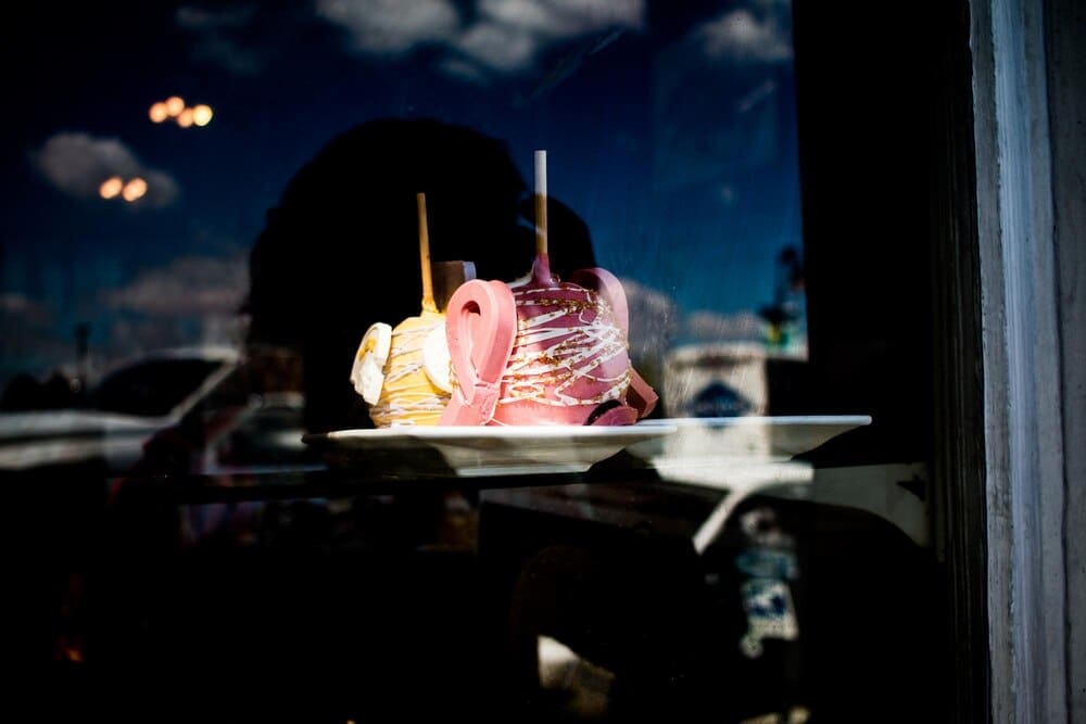 Close-up of a red candy apple on a white plate is seen through a window.