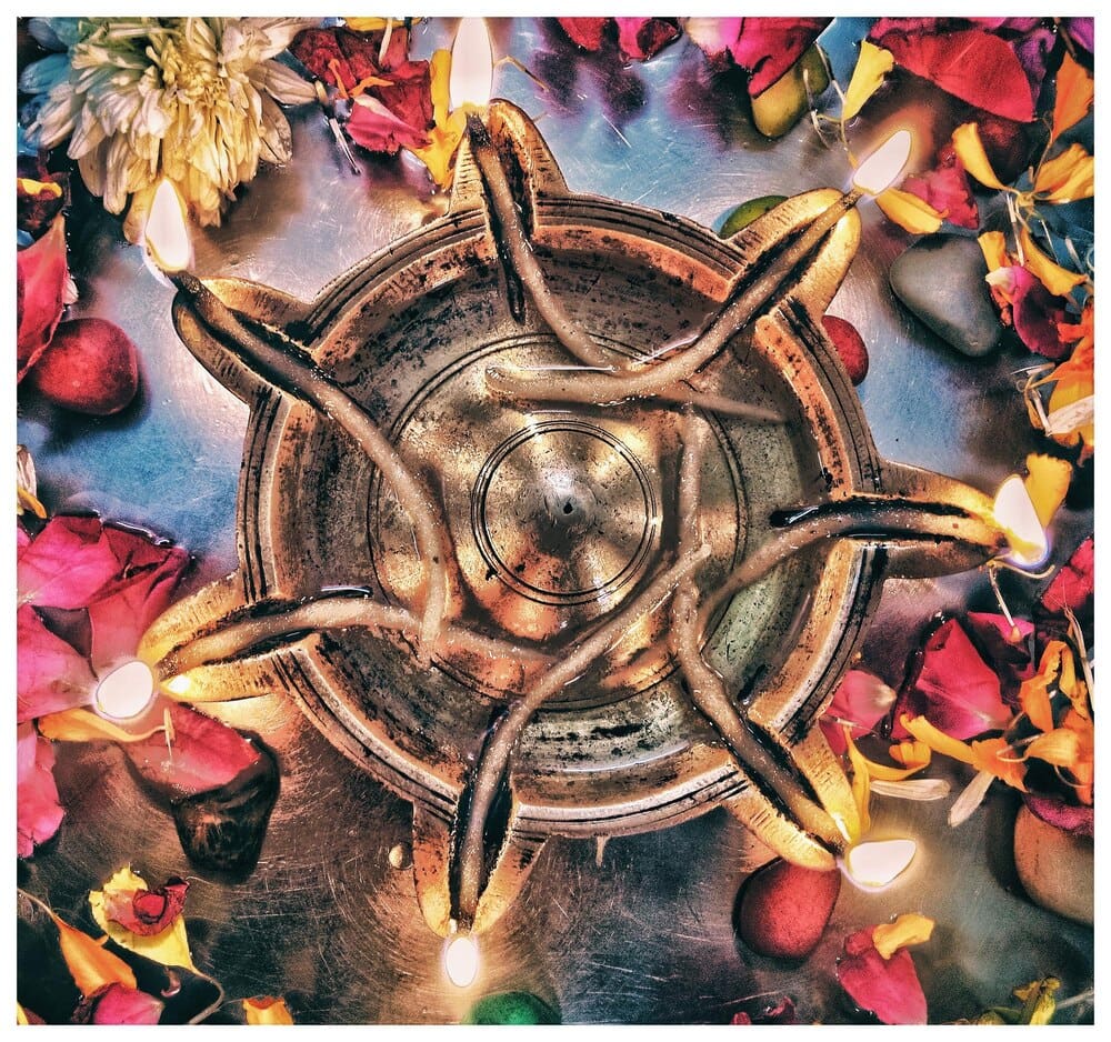Close-up of a small, lit oil lamp, or diya, surrounded by flower petals.