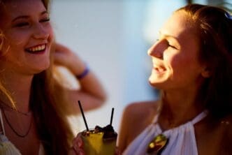 Two smiling women clink glasses filled with drinks.