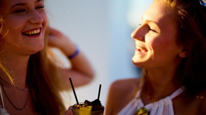 Two smiling women clink glasses filled with drinks.