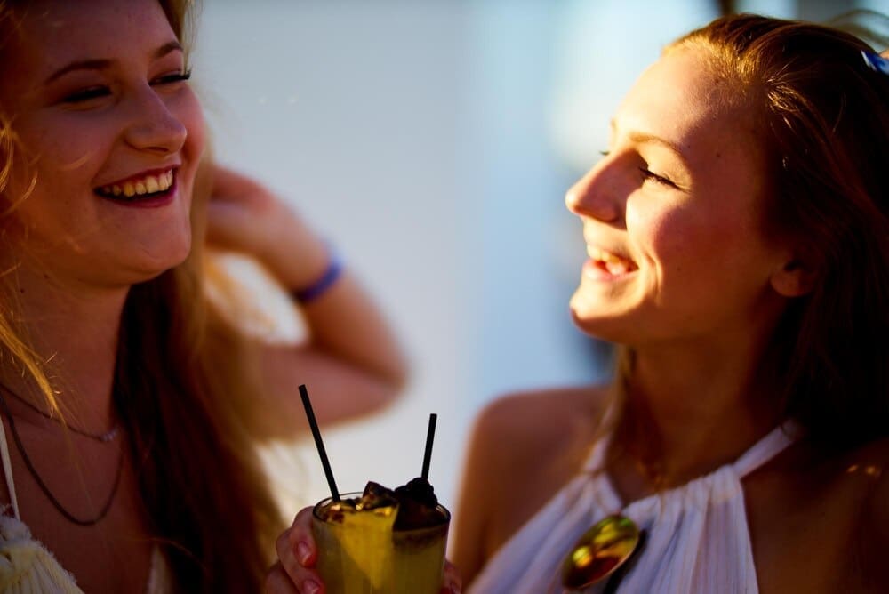 Two smiling women clink glasses filled with drinks.