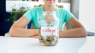 Close-up of a young woman in a t-shirt sitting at a white table with a jar labeled "credit" filled with coins.
