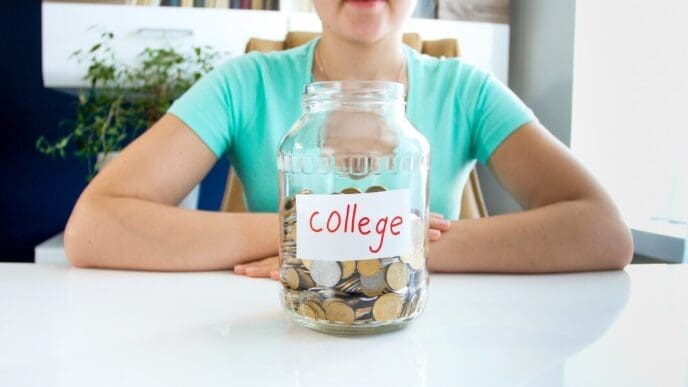Close-up of a young woman in a t-shirt sitting at a white table with a jar labeled "credit" filled with coins.