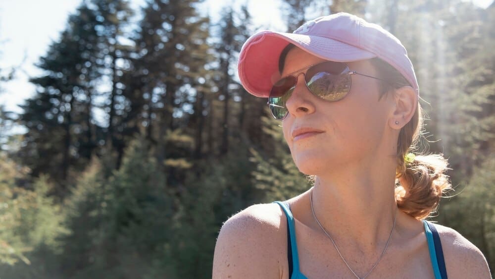 A woman with sunglasses poses for the camera in a close-up shot.