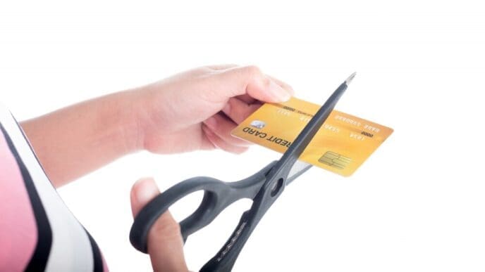 Close-up of a young woman's hand cutting a credit card with scissors against a pink background.