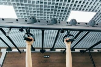 Close-up of a woman's hands gripping a pull-up bar in a gym.
