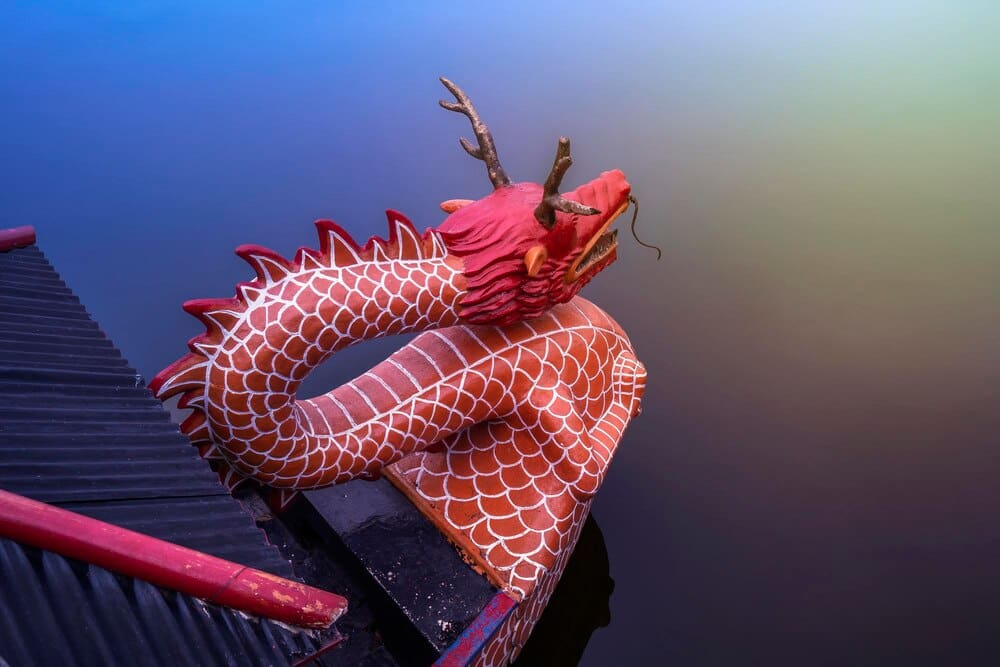 A close-up shot shows the front of a dragon boat on a lake, with decorative carvings and a colorful dragon head.