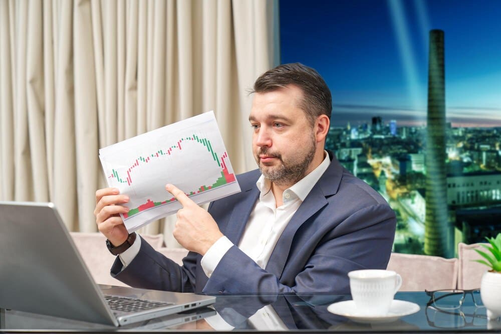 A financial coach leads an online investment training session, visible on a laptop screen, at a workplace.