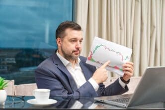 A coach leads an online financial investment training session, interacting with participants via a laptop at a workplace.