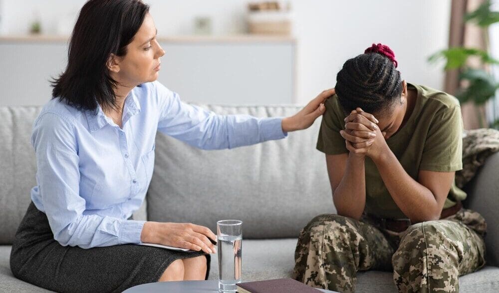 A psychologist comforts an African American military woman during a therapy session.
