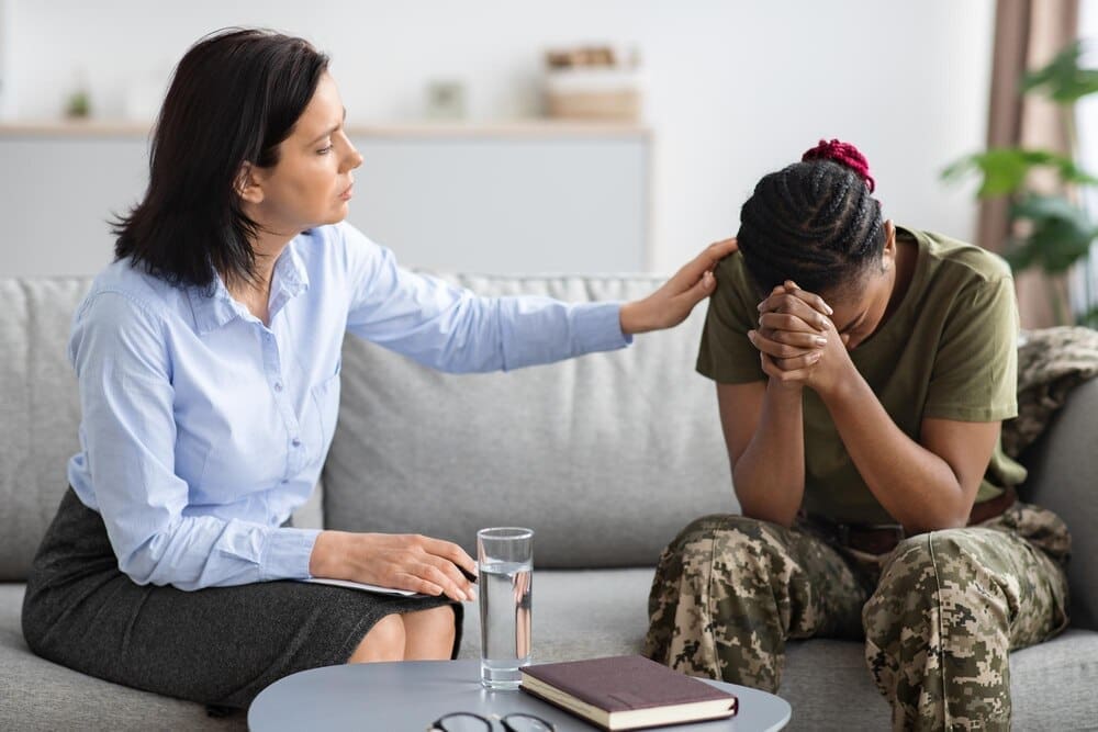 A psychologist comforts an African American military woman during a therapy session.