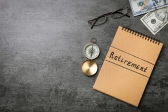 A notebook, compass, and money are arranged on a gray table, symbolizing financial planning.