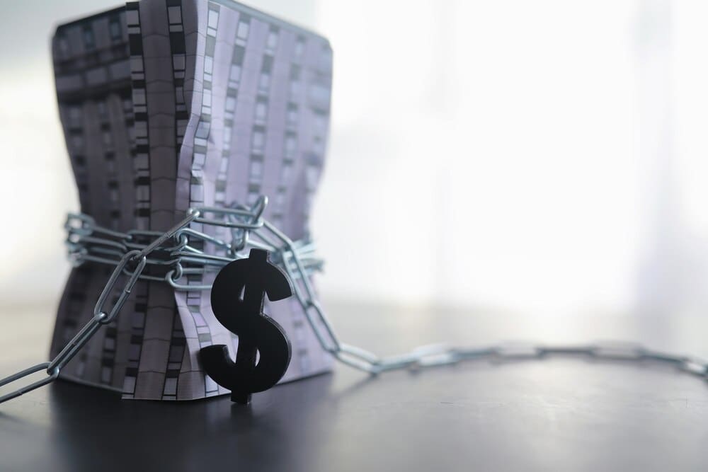 A house is being measured with a measuring tape that has a dollar sign, symbolizing financial dependence on borrowed funds and mortgage debt.
