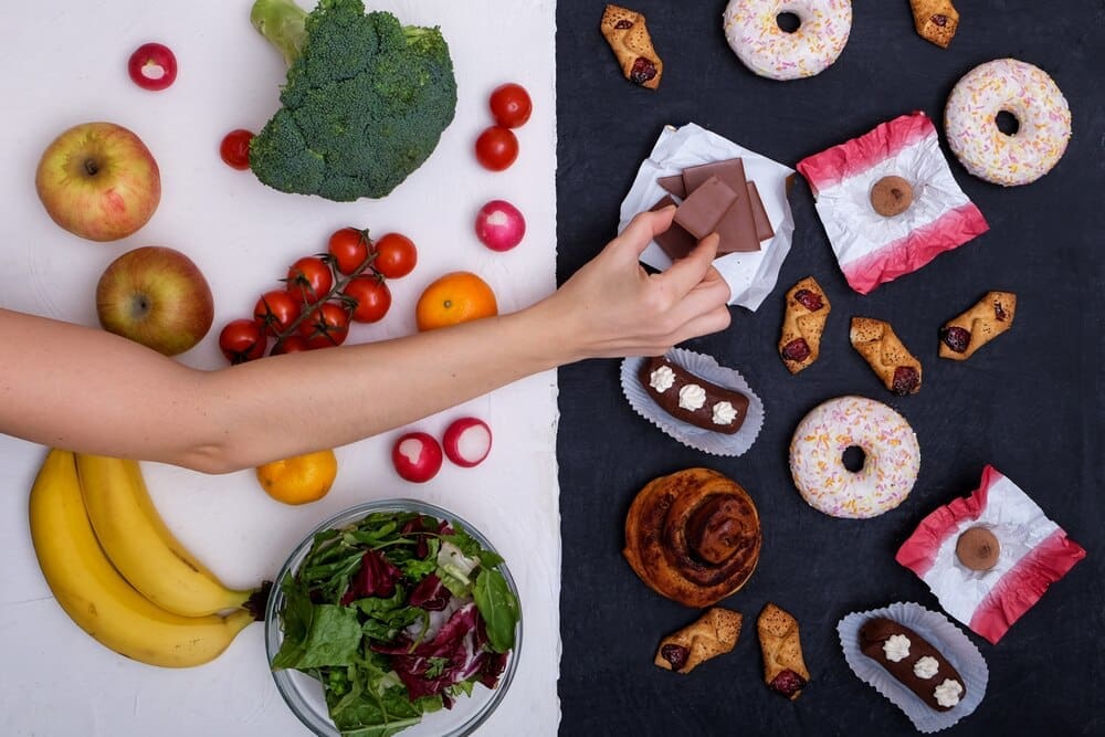 A split-screen image contrasts a selection of fresh fruits and vegetables with unhealthy options like donuts, sweets, and burgers.
