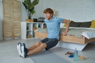 A young, red-haired man performs push-ups on a bed in a home setting, demonstrating fitness.