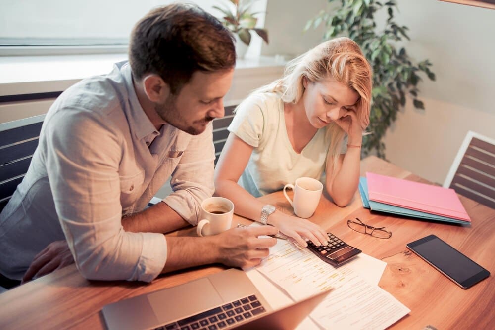 A couple reviews financial documents together while seated in their living room.