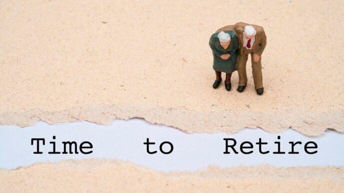 Miniature figures of an elderly couple stand next to the word "retire" on a brown paper background, representing retirement planning.
