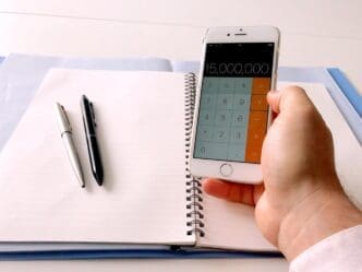 A person's hand uses a mobile phone to do calculations at home.