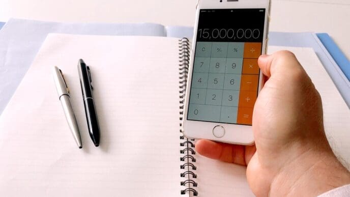 A person's hand uses a mobile phone to do calculations at home.
