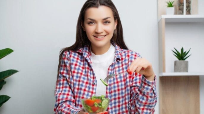 A smiling woman enjoys a fresh vegetable salad, emphasizing a healthy meal.