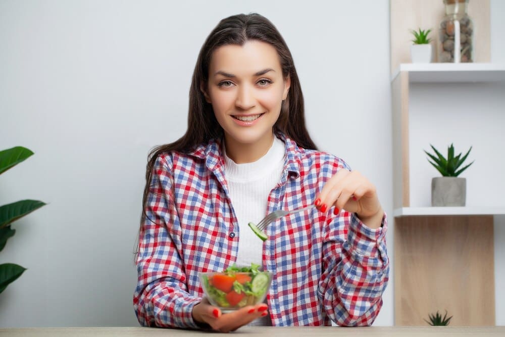 A smiling woman enjoys a fresh vegetable salad, emphasizing a healthy meal.