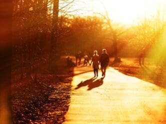 A couple holds hands and walks down a street at sunset, silhouetted against the colorful sky.