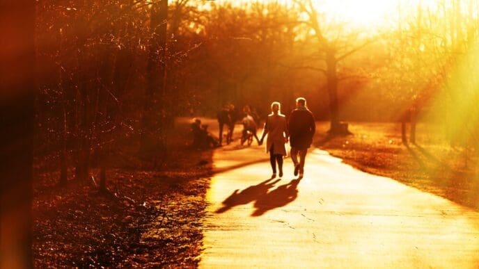 A couple holds hands and walks down a street at sunset, silhouetted against the colorful sky.