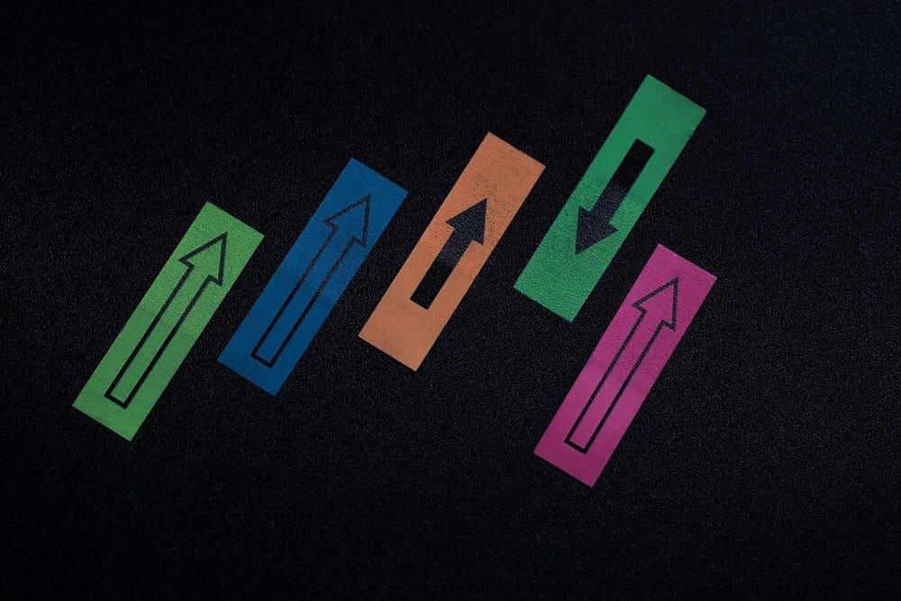 Overhead view of colorful arrow symbols pointing in opposing directions on a textured surface.