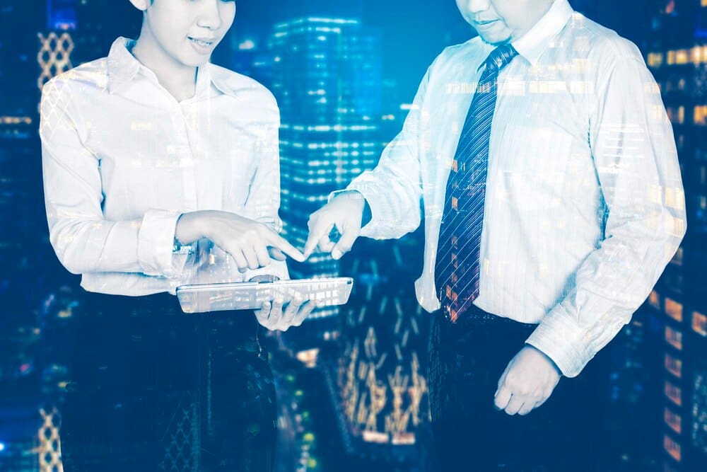 Double exposure shows two business people, one using a tablet, layered with the other.