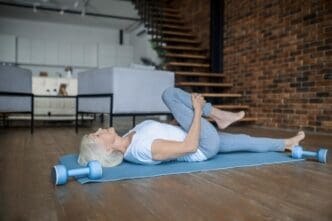 An elderly woman wearing workout clothes practices yoga in her home.